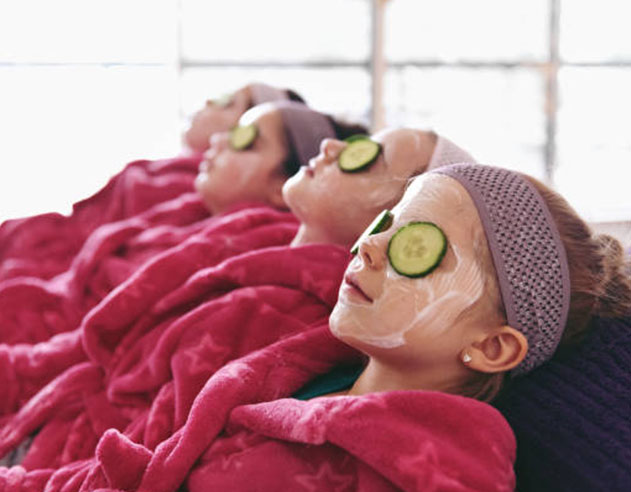 Young girls enjoy a fun spa session in pink robes, with facial masks and cucumber slices on their eyes, creating a playful and pampering experience